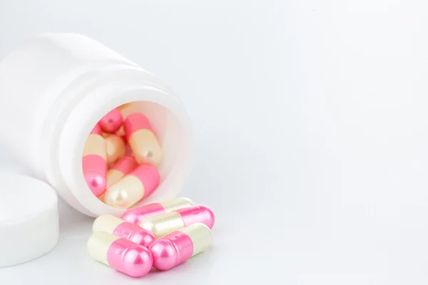 Pílulas de pérola rosa e amarela uma garrafa de pílula no fundo branco — Fotografia de Stock