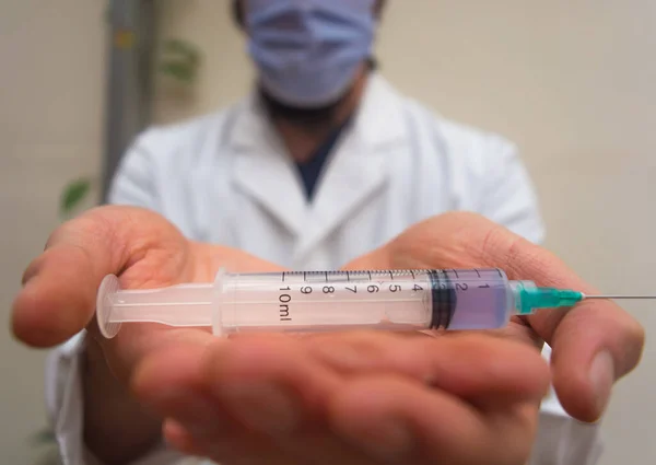 Beyaz önlüklü ve maskeli bir doktor tek kullanımlık plastik şırıngayı elinde tutarak elinde iğne ve mavi sıvıyı aşı olarak kullanıyordu. Aşı için hazırlanıyor COVID-19 veya koronavirüs sahnesi