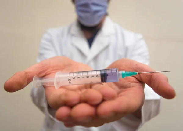 Beyaz önlüklü ve maskeli bir doktor tek kullanımlık plastik şırıngayı elinde tutarak elinde iğne ve mavi sıvıyı aşı olarak kullanıyordu. Aşı için hazırlanıyor COVID-19 veya koronavirüs sahnesi