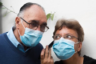 Yaşlı bir çiftin portresi, erkek ve kadın, tıbbi yüz maskesi ve beyaz arka planda konuşan gözlük kullanıyorlar. COVID ya da koronavirüs salgını sırasında yeni normallik sahnesi