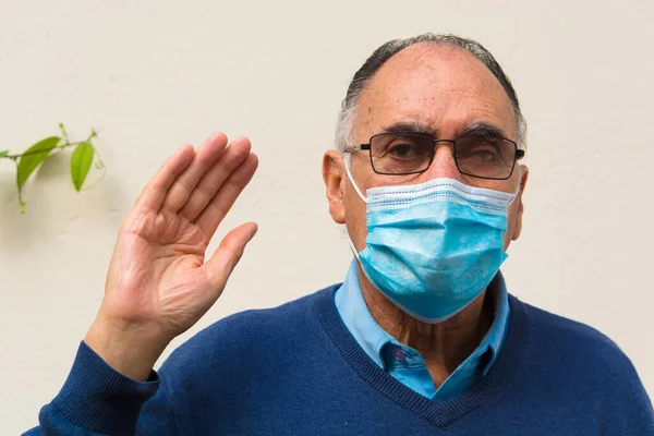 Portrait of a doctor old senior man wearing glasses and medical face mask, looking at camera doing a peace hand sign.Scene of COVID 19 OR coronavirus pandemic