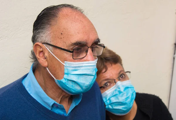 Tıbbi maske ve beyaz arka planda gözlük takan yaşlı bir çiftin portresi. Aşk ve anlayış dışavurumu. COVID ya da koronavirüs salgını sırasında yeni normallik sahnesi