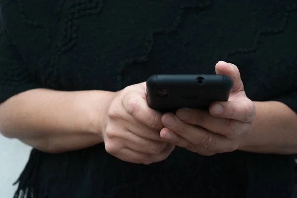 Sohbet etmek için sosyal medya uygulamaları kullanarak akıllı telefon ya da cep telefonu tutan eller. Arka planda siyah kıyafetler var.