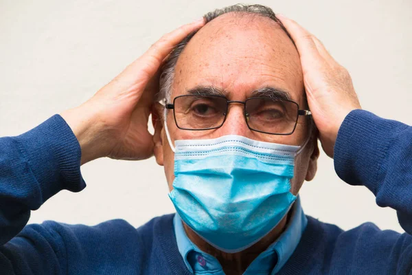 Gözlük takan yaşlı bir doktorun portresi ve tıbbi yüz maskesi, endişeli bir şekilde kameraya bakıyor. COVID 19 ya da Coronavirus salgınının sahnesi.