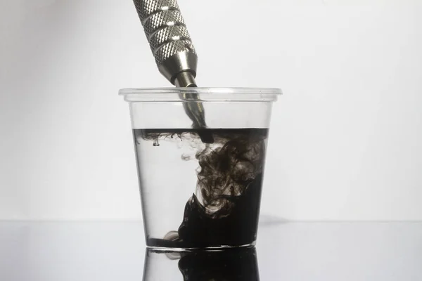 透明なガラスの中にきれいな水で黒いインクの針をきれいにタトゥーマシン — ストック写真