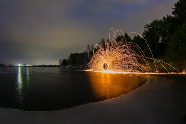 Gnistor från den brinnande stålullen mot bakgrund av en frusen sjö våren natt — Stockfoto