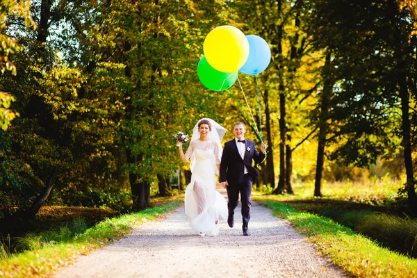 A noiva e o noivo correndo pelo beco com balões — Fotografia de Stock