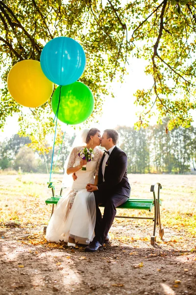 A noiva e o noivo sentam-se no banco com balões — Fotografia de Stock