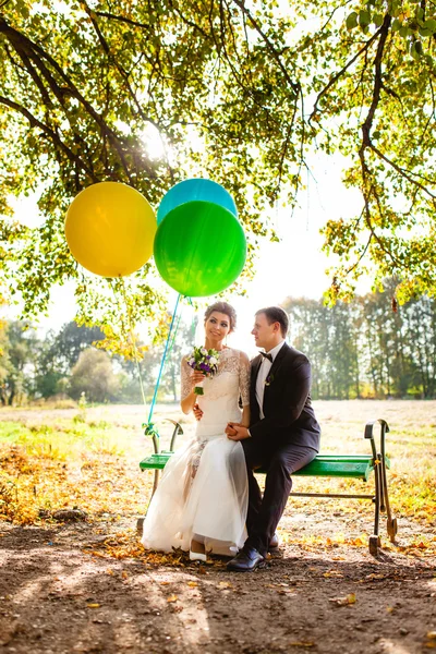 De bruid en bruidegom zitten op de Bank met ballonnen — Stockfoto
