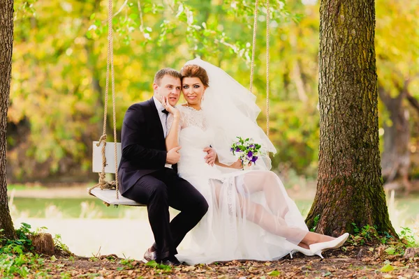 Das Brautpaar auf einer Schaukel vor dem Hintergrund der herbstlichen Landschaft — Stockfoto