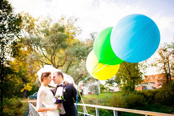 Braut und Bräutigam umarmen sich auf der Brücke mit Luftballons — Stockfoto
