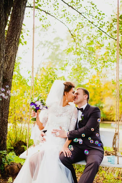 A noiva e o noivo em um balanço e bolhas voadoras — Fotografia de Stock
