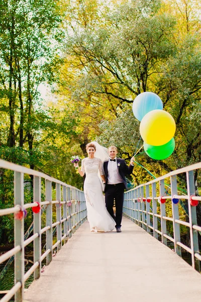 Narzeczeni są spacery na moście z balonów na tle jesień krajobraz — Zdjęcie stockowe