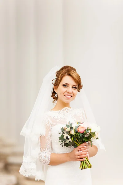 Ritratto di una bella giovane sposa che si erge tra le colonne e regge un bouquet da sposa — Foto Stock