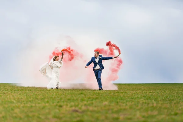 De bruid en bruidegom loopt door het gebied met rode rook bommen — Stockfoto