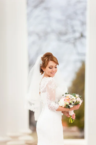 Giovane bella sposa in piedi tra i pilastri e in possesso di un bouquet da sposa — Foto Stock