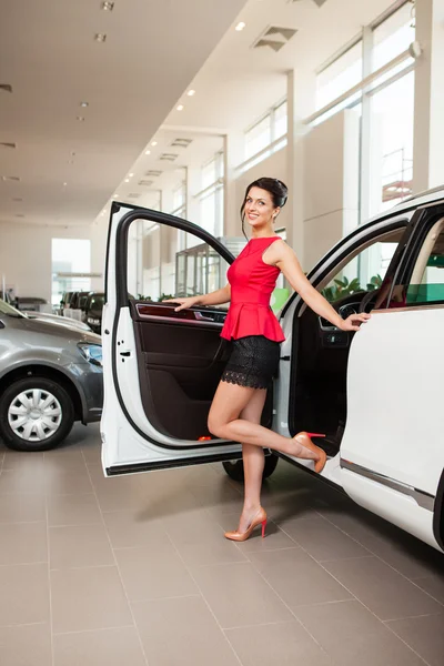 Kısa etekli güzel kız beyaz bir araba showroom yanında duruyor