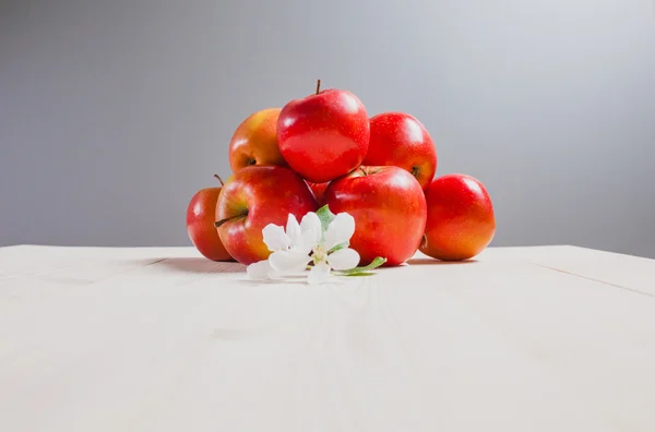 Unas manzanas rojas sobre una mesa blanca con flores — Foto de Stock