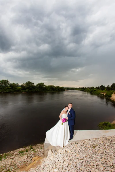 Le marié embrasse la mariée sur la rive de la rivière — Photo