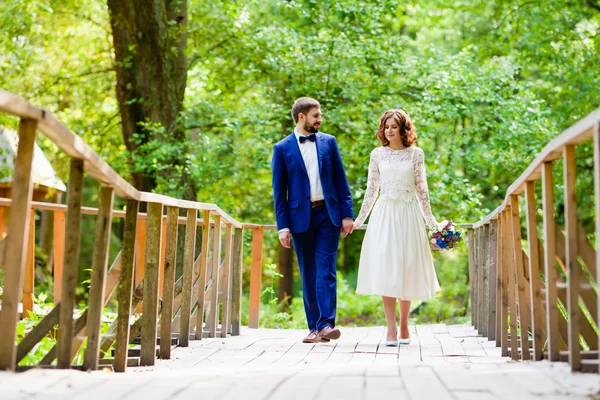 Bruden och brudgummen gå på en träbro — Stockfoto