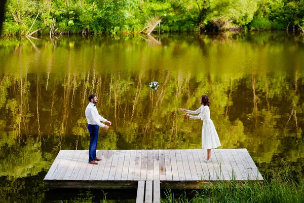 Le marié jetant bouquet nuptial à la mariée près du lac — Photo