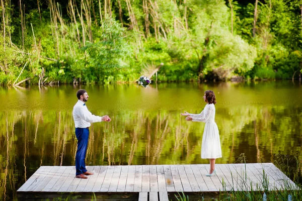 Der Bräutigam wirft der Braut den Brautstrauß in der Nähe des Sees — Stockfoto