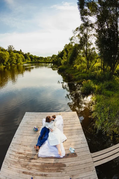 Braut und Bräutigam liegen auf einem hölzernen Steg am Teich — Stockfoto
