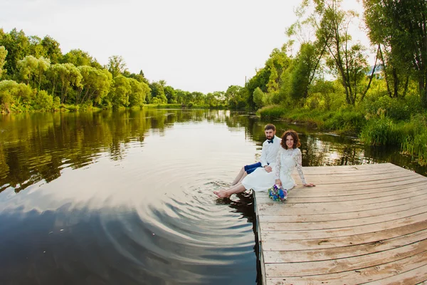 Les mariés sont assis sur une jetée en bois près de l'étang — Photo
