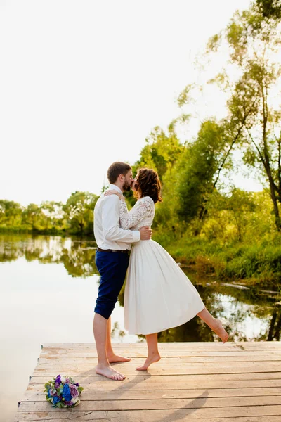 Η νύφη και ο γαμπρός στέκονται σε μια ξύλινη αποβάθρα κοντά στη λίμνη — Φωτογραφία Αρχείου