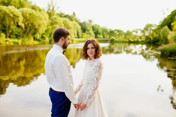 Bruden och brudgummen står på en träbrygga nära dammen — Stockfoto