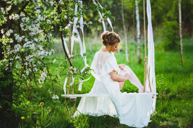 Sarı saçlı, beyaz gecelikli ve çoraplı gelin jartiyer giyiyor.