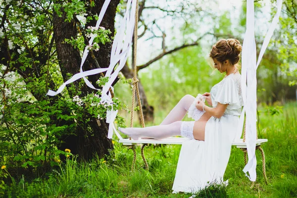 Junge Braut mit blonden Haaren in weißem Negligee und Strümpfen mit Strumpfband — Stockfoto