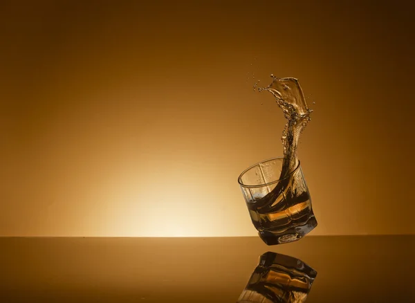Padající sklenici whisky na zlaté pozadí — Stock fotografie