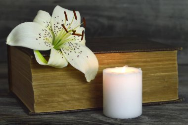 Beyaz mumlu sempati kartı, zambak çiçeği ve kapalı kitap.  