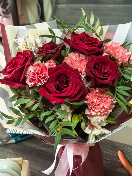 Bir buket kırmızı gül, karanfil ve okaliptüs bir vazo içinde ahşap bir çiçek masasında. Paketlenmiş buket