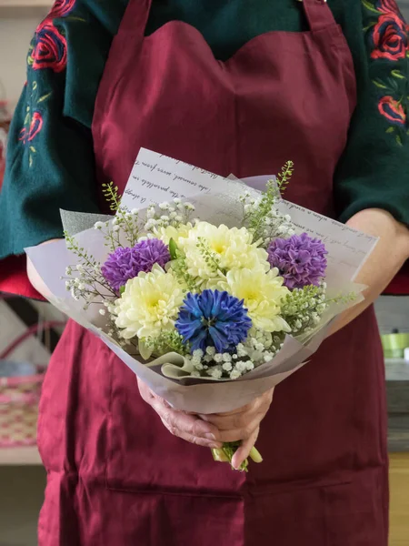 In the hands of the florist, a bouquet of yellow chrysanthemums and blue, purple hyacinths. Wrapped bouquet. Background apron at the florist fuchsia color