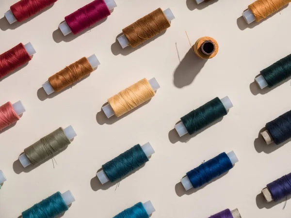 The multi-colored spools of thread lie in a row diagonally. A repeating pattern. Sewing thread texture. Hard light. Beautiful sewing items. Sewing thread spools. View from above