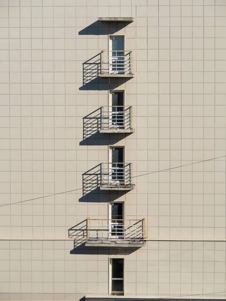 The wall of the facade of a multi-storey building with balconies, plastic windows and doors. The shadow from the balconies in a multi-storey building creates an additional reality. Unusual texture. Wallpaper and background.