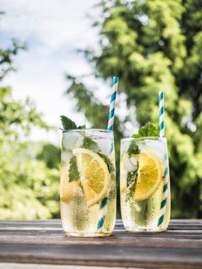 Buzlu, limonlu ve şeffaf bir bardakta üzümlü soğuk karbonatlı limonata. Yaz içeceği bahçedeki ahşap bir masada duruyor. Arkaplan - köknar dalları
