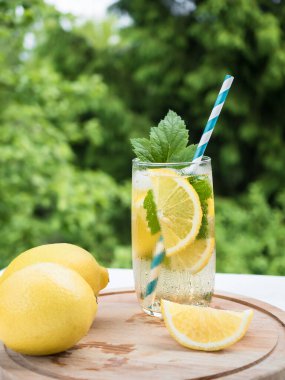 Tahta tepside buzlu ve limonlu soğuk limonata. Bahçede yaz içkisi. Arkaplan - ağaçların yeşil dalları.