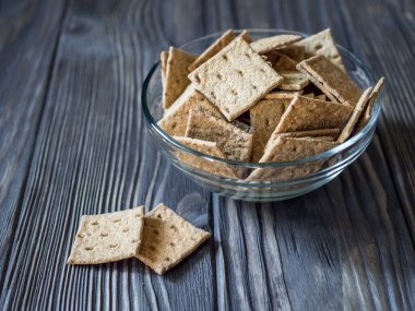 Koyu ahşap arka planda cam bir kasede doğal çıtır mini ekmekler. Ahşap dokular. Diyet atıştırmalık