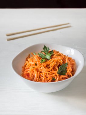 Baharatlı Asya salatası, rendelenmiş havuç ve maydanoz. Beyaz arka planda çubukları olan beyaz bir kâsede Kore havuçları. Vejetaryen diyeti. Sağlıklı gıda konsepti. Dikey