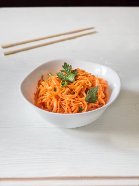 Baharatlı Asya salatası, rendelenmiş havuç ve maydanoz. Beyaz arka planda çubukları olan beyaz bir kâsede Kore havuçları. Vejetaryen diyeti. Sağlıklı gıda konsepti. Dikey