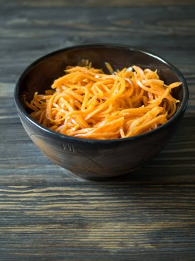 Baharatlı Asya salatası ve rendelenmiş havuç. Kahverengi ahşap arka planda koyu bir kasede Kore havuçları. Vejetaryen diyeti. Sağlıklı gıda konsepti. Dikey. Boşluğu kopyala. 