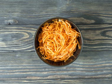 Baharatlı Asya salatası ve rendelenmiş havuç. Kahverengi ahşap arka planda koyu bir kâsede Kore havucu. Vejetaryen diyeti. Sağlıklı gıda konsepti. Düz yatıyordu. Yatay olarak. Yukarıdan bak. Boşluğu kopyala