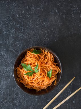 Baharatlı Asya salatası, rendelenmiş havuç ve maydanoz. Siyah arka planda, sade, yemek çubukları ve tekstil ile siyah bir kâsede Kore havuçları. Vejetaryen diyeti. Sağlıklı gıda konsepti. Yukarıdan bak. Düz yatıyordu