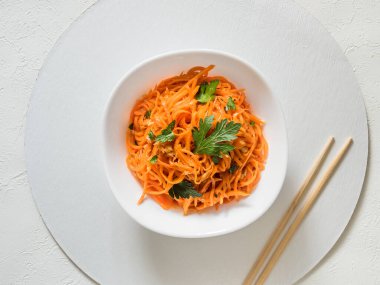 Baharatlı Asya salatası, rendelenmiş havuç ve maydanoz. Siyah arka planda, sade, yemek çubukları ve tekstil ile siyah bir kâsede Kore havuçları. Vejetaryen diyeti. Sağlıklı gıda konsepti. Yukarıdan görüntüle