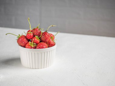 Bahçeden toplanan taze kırmızı böğürtlen. Beyaz bir masada beyaz bir kasede çilek. Masa çapraz duruyor. Arka planda beyaz süslemeli tuğla. Vejetaryen atıştırması. Yatay olarak