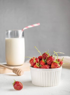 İştah açıcı taze çilek ve yeşil pirzola beyaz arka planda beyaz bir kasede duruyor. Arka planda pipet olan bir bardak süt. Kahvaltı konsepti. Ev rahatlığı. Dikey