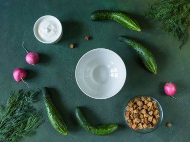 Geleneksel soğuk Rus çorbası-okroshka haşlanmış yumurta ve otlarla süslenmiş, masada beyaz bir kraker, ekşi krema ve çorba malzemeleriyle birlikte. Yeşil arka plan. Üst Manzara. Yatay olarak